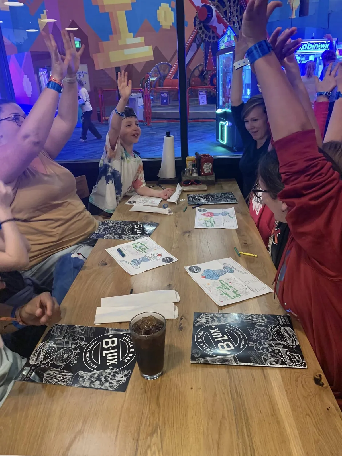 Children and adults sit together at a table in a colorful activity venue